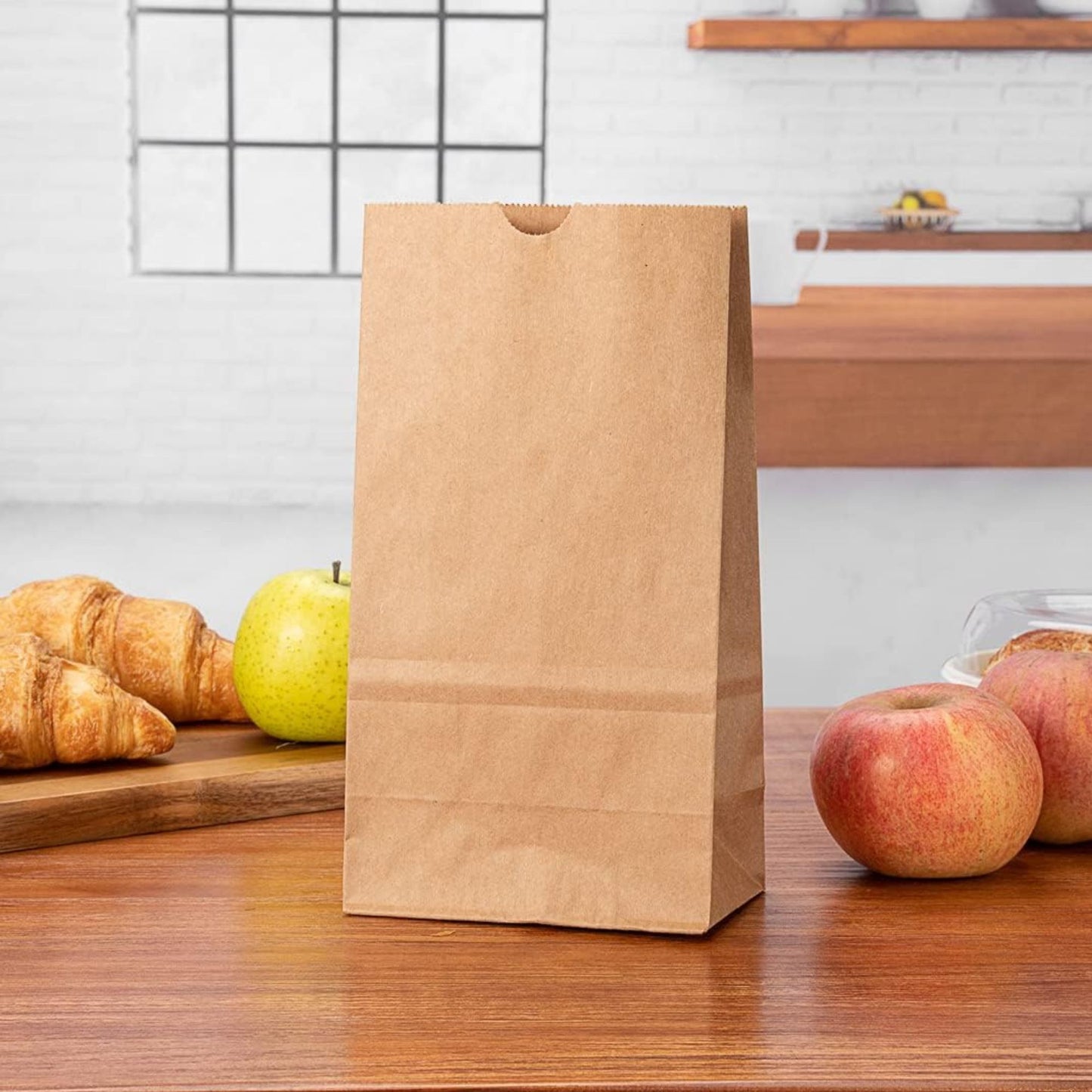 Brown paper bag on a wooden table with apples and croissants in the background.