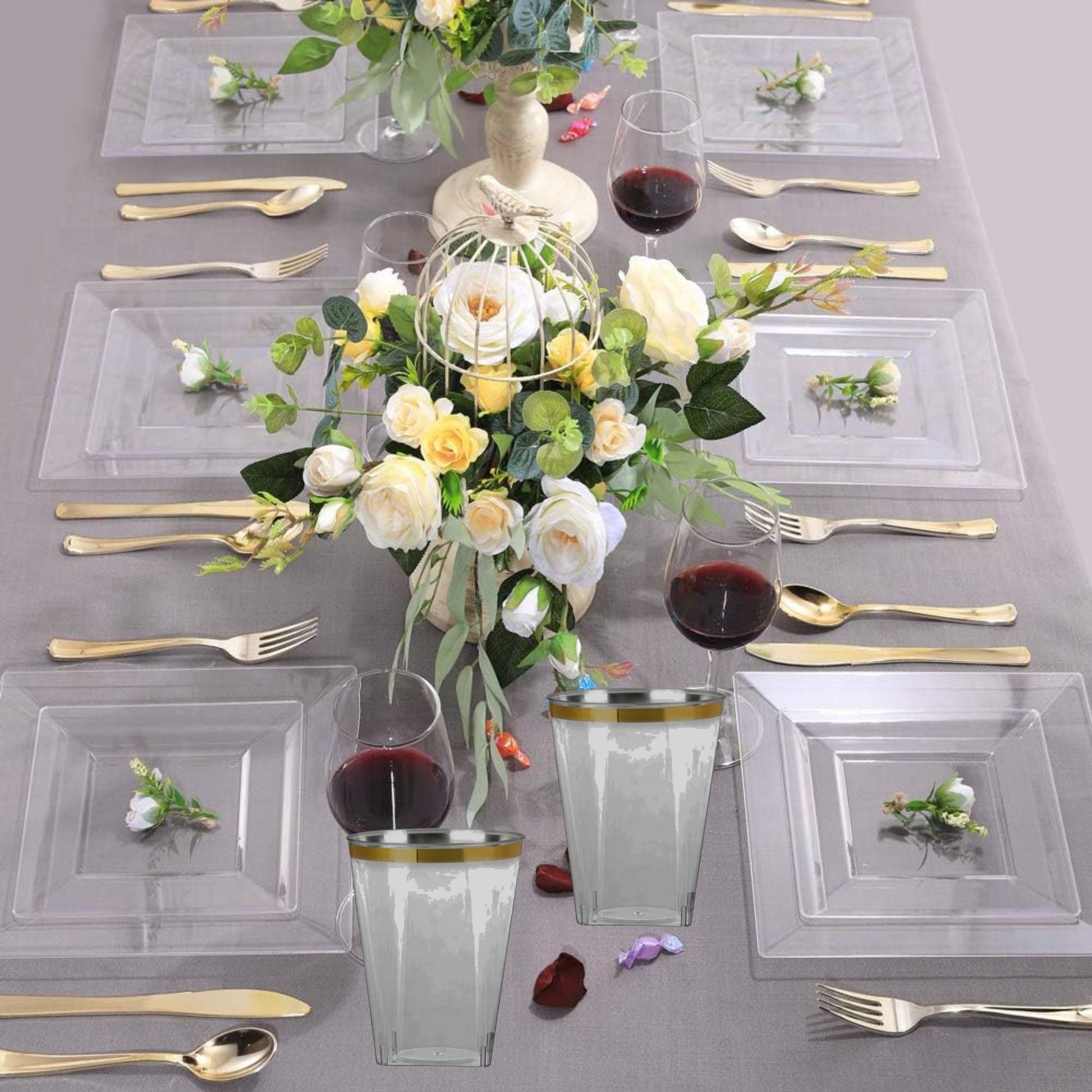 Elegant table setting with clear glassware, gold cutlery, and floral centerpieces on a gray tablecloth.