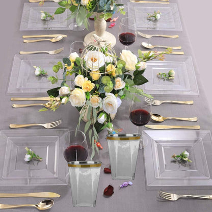 Elegant table setting with clear glassware, gold cutlery, and floral centerpieces on a gray tablecloth.