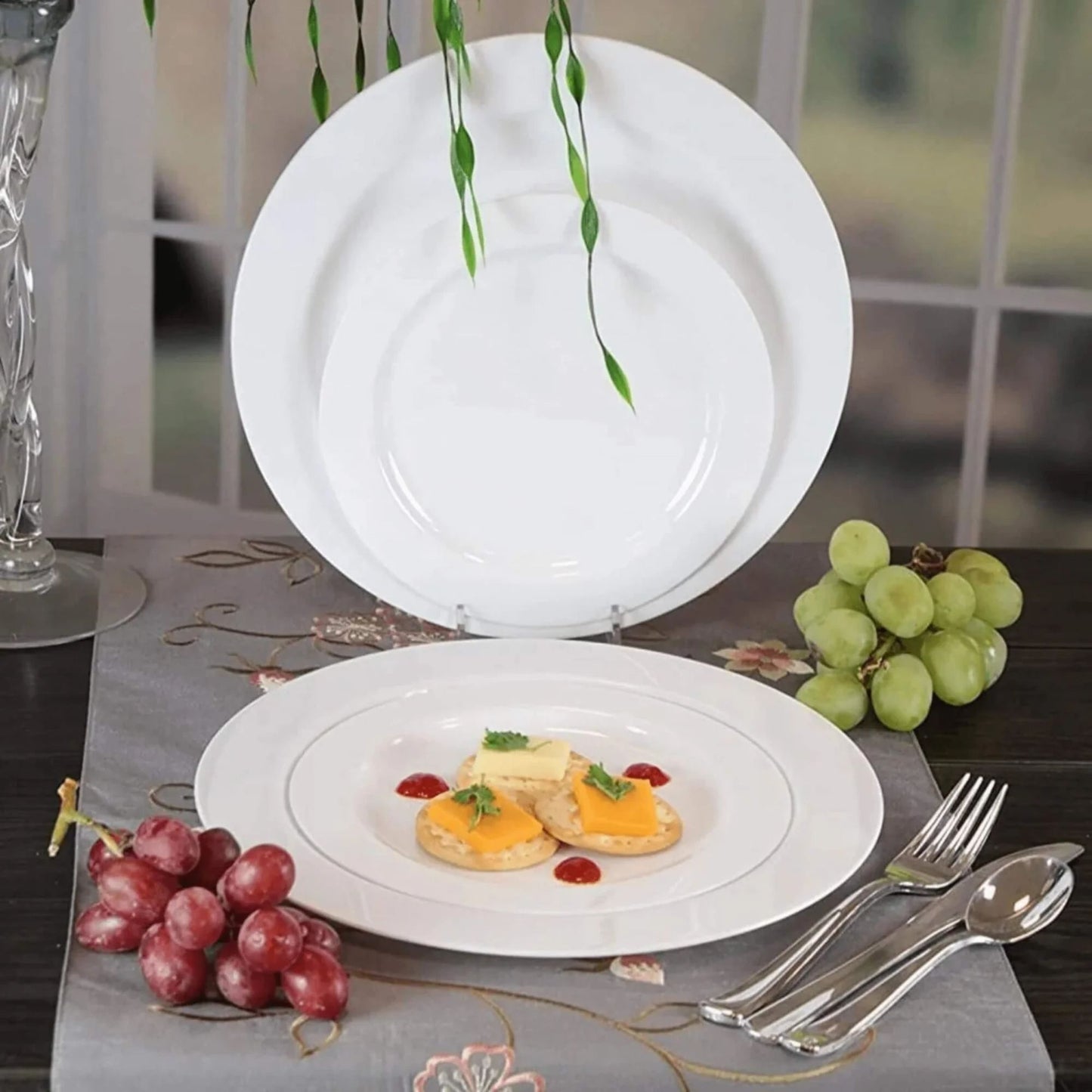 White ceramic plates with food on a table setting with grapes and cutlery.