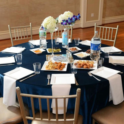 Round table set for a formal event with navy tablecloth, white napkins, and food.