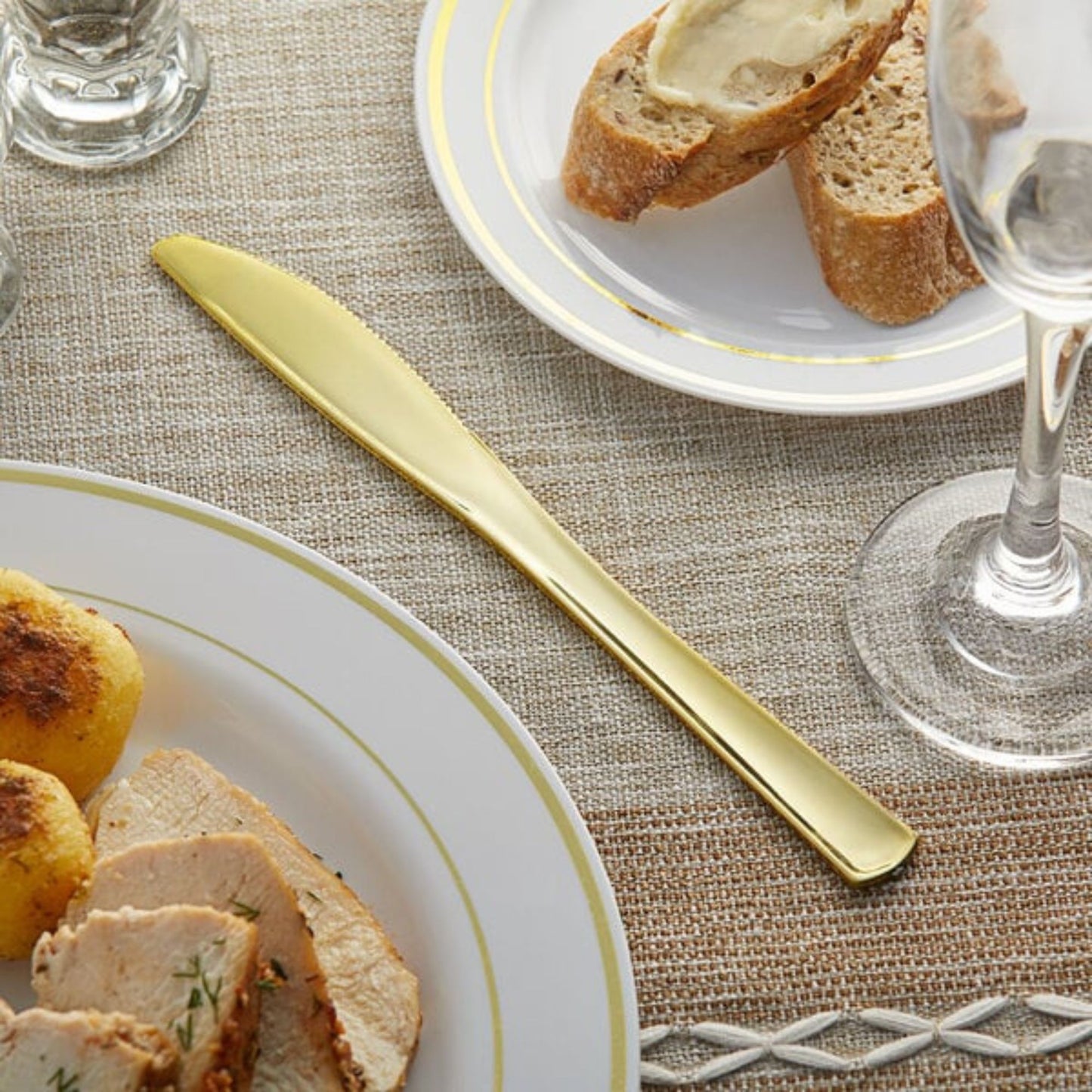 Gold knife on a table with plates of food, bread, and glasses.