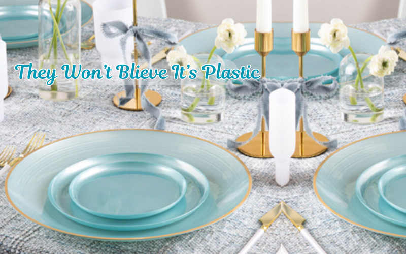 Table setting with blue plates, gold cutlery, and white flowers on a gray tablecloth.